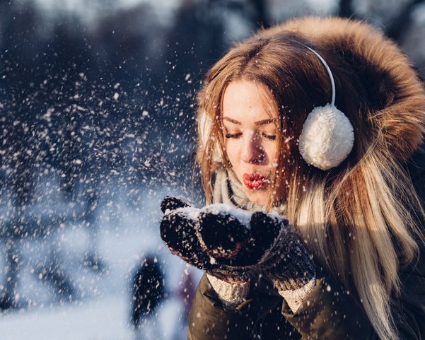 Eine Frau in Winterkleidung pustet Schnee in ihren Händen weg