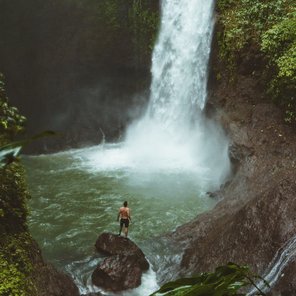 Mann vor Wasserfall im Dschungel