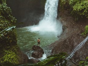 Mann vor Wasserfall im Dschungel