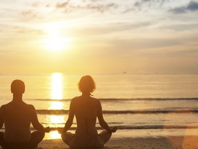 Ein junges Prächen meditiert an der Küste bei Sonnenuntergang