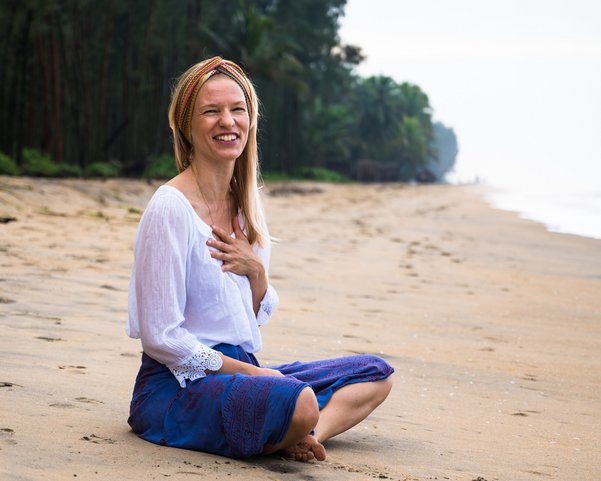 Eine blonde Frau sitzt lachend an einem Strand