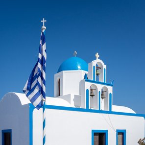 Eine weiße Kirche mit blauem Rand und einem runden Dach mit griechischer Flagge davor