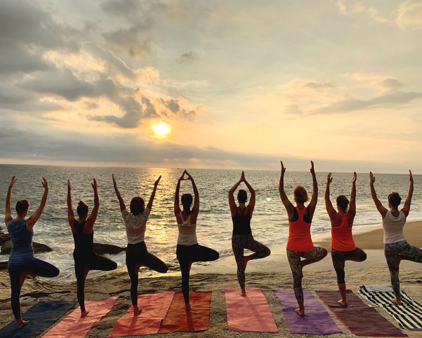 Frauen nebeneinander in der Baum Pose am Strand