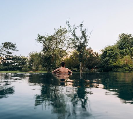 Mann im Pool schaut in die grüne Landschaft mit Bäumen