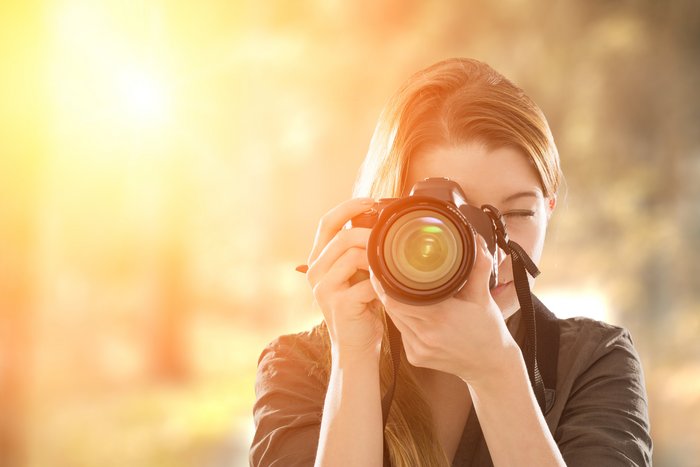 Eine Frau hält ein Fotoapparat in ihr Gesicht um etwas zu fotografieren