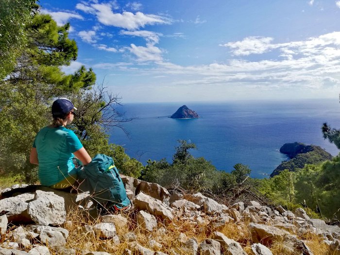 Eine Frau sitzt auf einem steinigen Weg und blickt auf einen Felsen mitten im offenen Meer
