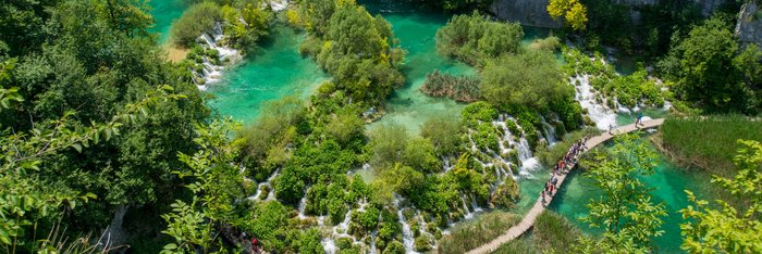 Ein See mit vielen kleinen Wasserfällen und Bäumen durch den ein Steg führt