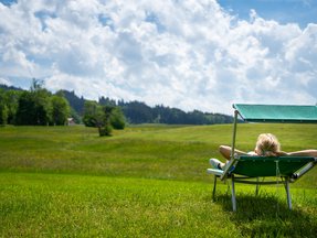 Eine Frau liegt auf einer grünen Weide und sonnt sich auf einer Sonnenliege