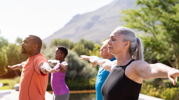 Eine Gruppe an älteren Menschen übt Yoga mit ausgestreckten Armen