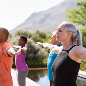 Eine Gruppe an älteren Menschen übt Yoga mit ausgestreckten Armen
