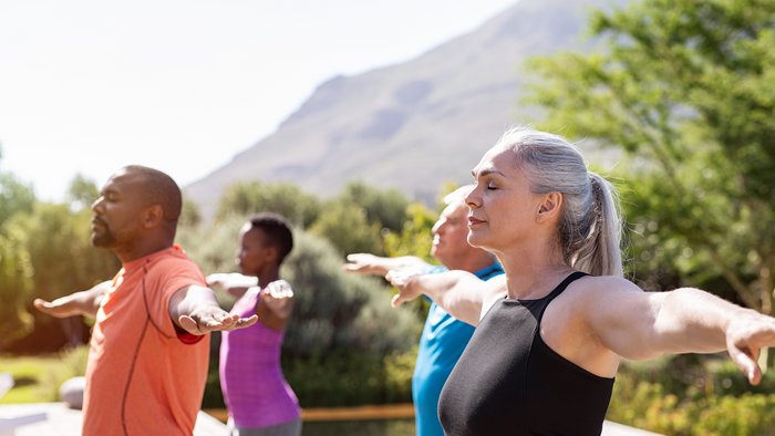 Eine Gruppe an älteren Menschen übt Yoga mit ausgestreckten Armen