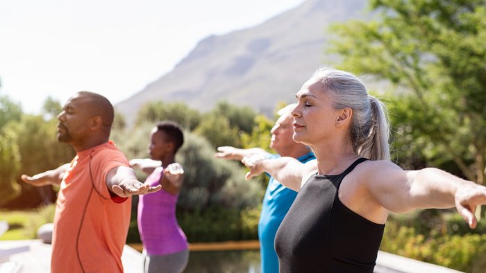 Eine Gruppe an älteren Menschen übt Yoga mit ausgestreckten Armen