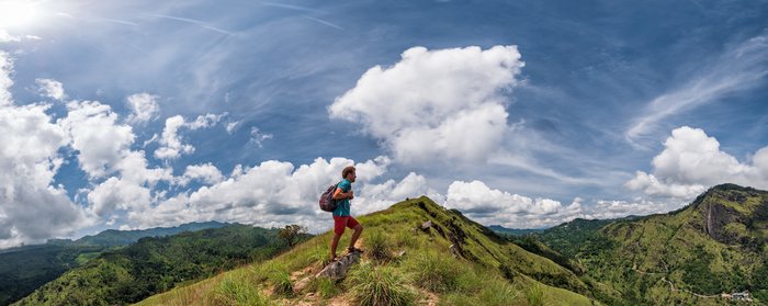 Ein Wanderer besteigt einen grünen Gipfel bei blauem Himmel