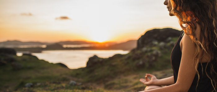 Eine Frau übt in Lotusposition Yoga in der Natur