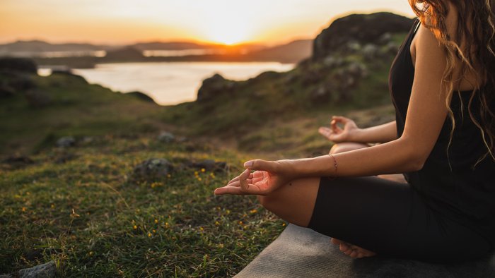 Eine Frau übt in Lotusposition Yoga in der Natur
