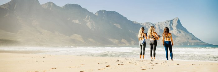 Rückansicht dreier junger Frauen auf der Suche nach einem Platz am Strand, um Yoga zu praktizieren