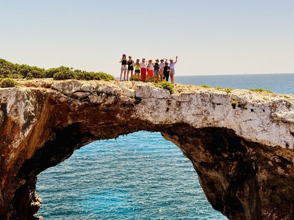 Eine Gruppe Menschen steht auf einem Bogen aus Fels über dem Meer