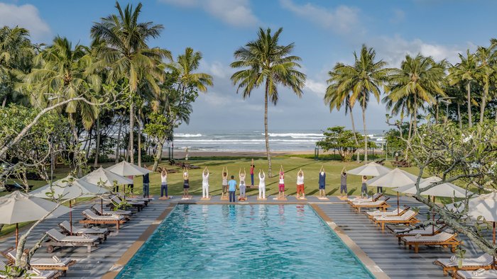 Eine Gruppe übt Yoga an einem Pool mit Blick auf das Meer