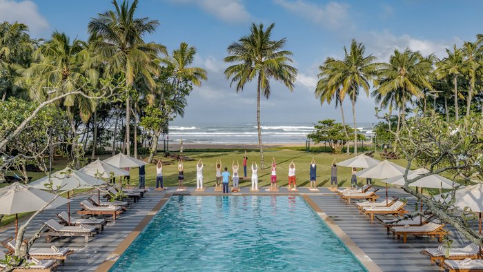 Eine Gruppe übt Yoga an einem Pool mit Blick auf das Meer