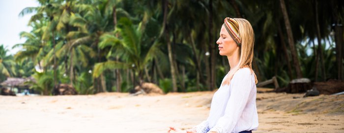 Eine junge Frau sitzt im Sukhasana an einem Strand
