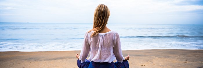 Eine blonde Frau übt Meditation an einem Strand