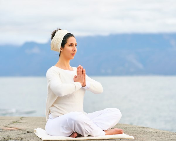 Eine Frau übt Meditation an einem See in weißer Bekleidung
