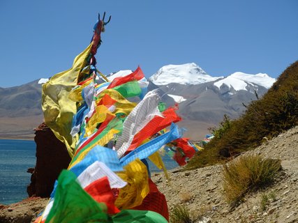 Bunte Fahnen, blaues Leuchten - der Manasarovar See hebt sich zwischen den Felsen am Berg Kailash ab