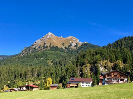 Mehrere Gebäude in einem Tal mit vielen Bäumen, grüner Wiese und großen Bergen