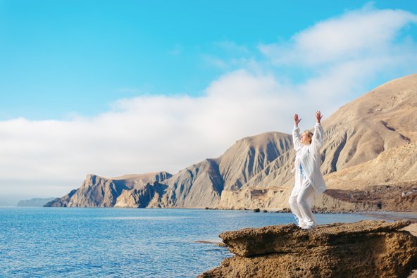 Eine Frau übt Tai Chi auf einem Felsen am Meer