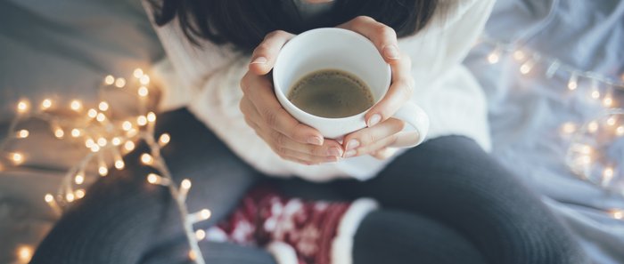 Eine Frau sitzt im Schneidersitz auf dem Bett mit einer Tasse Kaffee